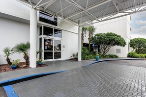 A modern building entrance with a covered walkway, palm trees, and a brick-paved area. - New Gulf-Front Listing| Amazing Views| Pools| Tennis Courts| Gym| Free Rounds of Golf (Pensacola)