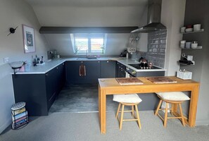 Une cuisine moderne dotée d’un îlot central, d’une table à manger avec des tabourets et d’une fenêtre laissant entrer la lumière naturelle.