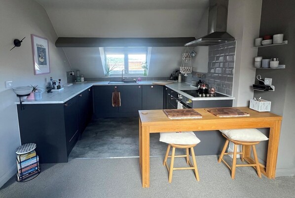 Cocina moderna con una isla central, una mesa de comedor con taburetes y una ventana que proporciona luz natural.