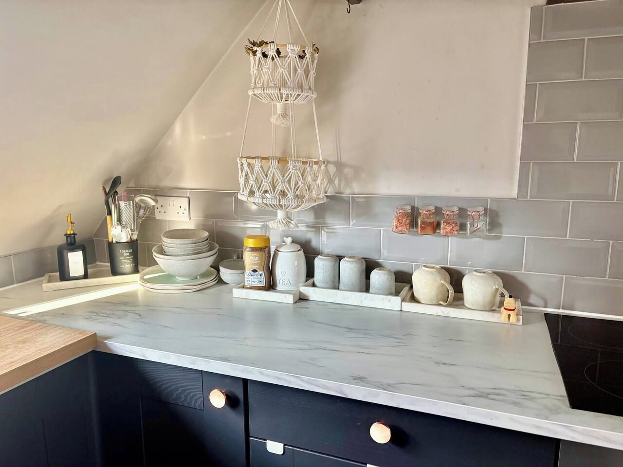 Una cocina con encimera de mármol, lámpara colgante de macramé y salpicadero de azulejos.
