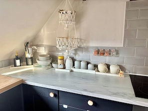 A kitchen with a marble countertop, a hanging macrame light fixture, and a tiled backsplash.