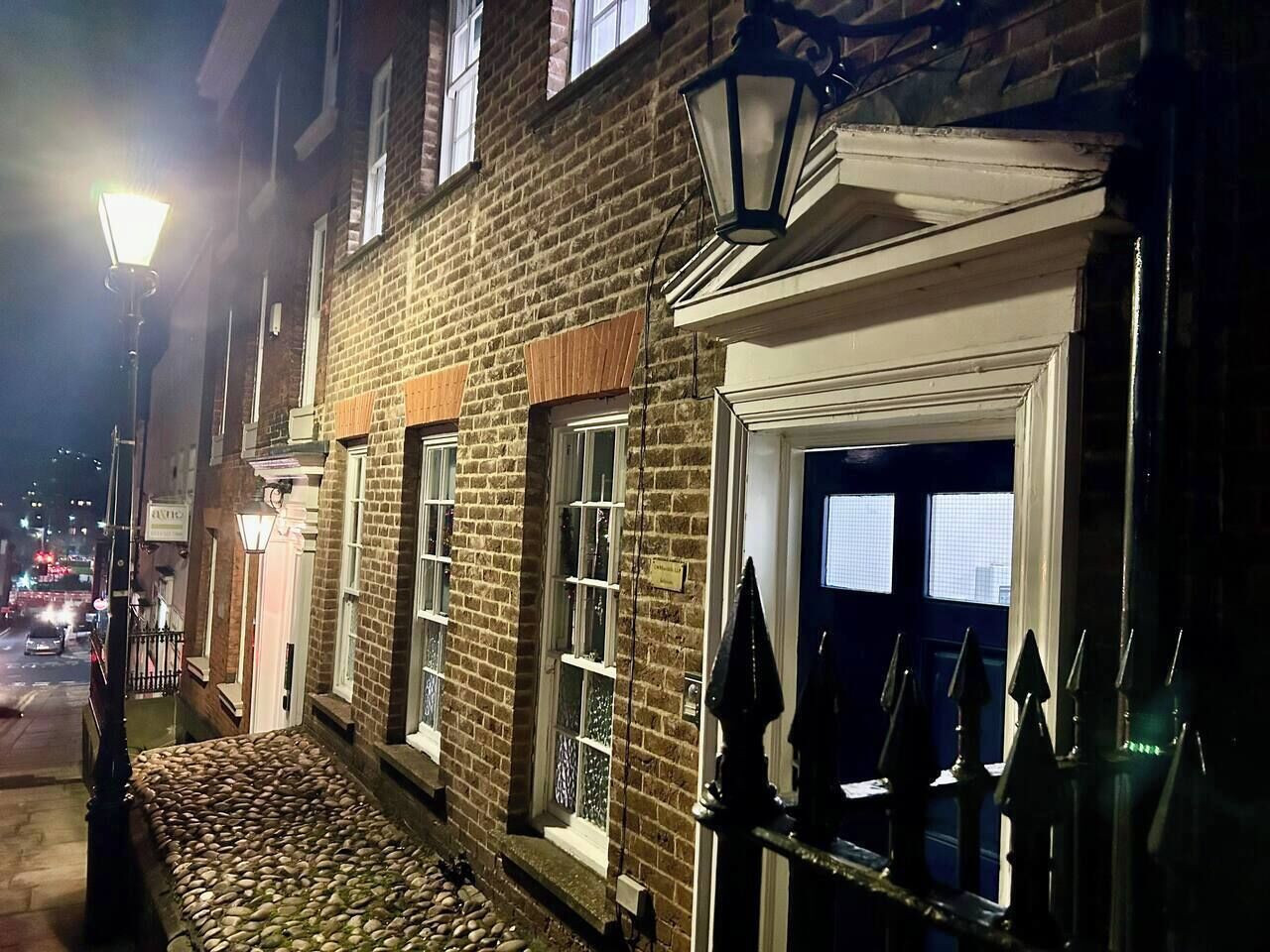 A brick building with a cobblestone entrance, a gated door, and a street lamp.