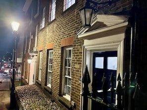 A brick building with a cobblestone entrance, a gated door, and a street lamp.