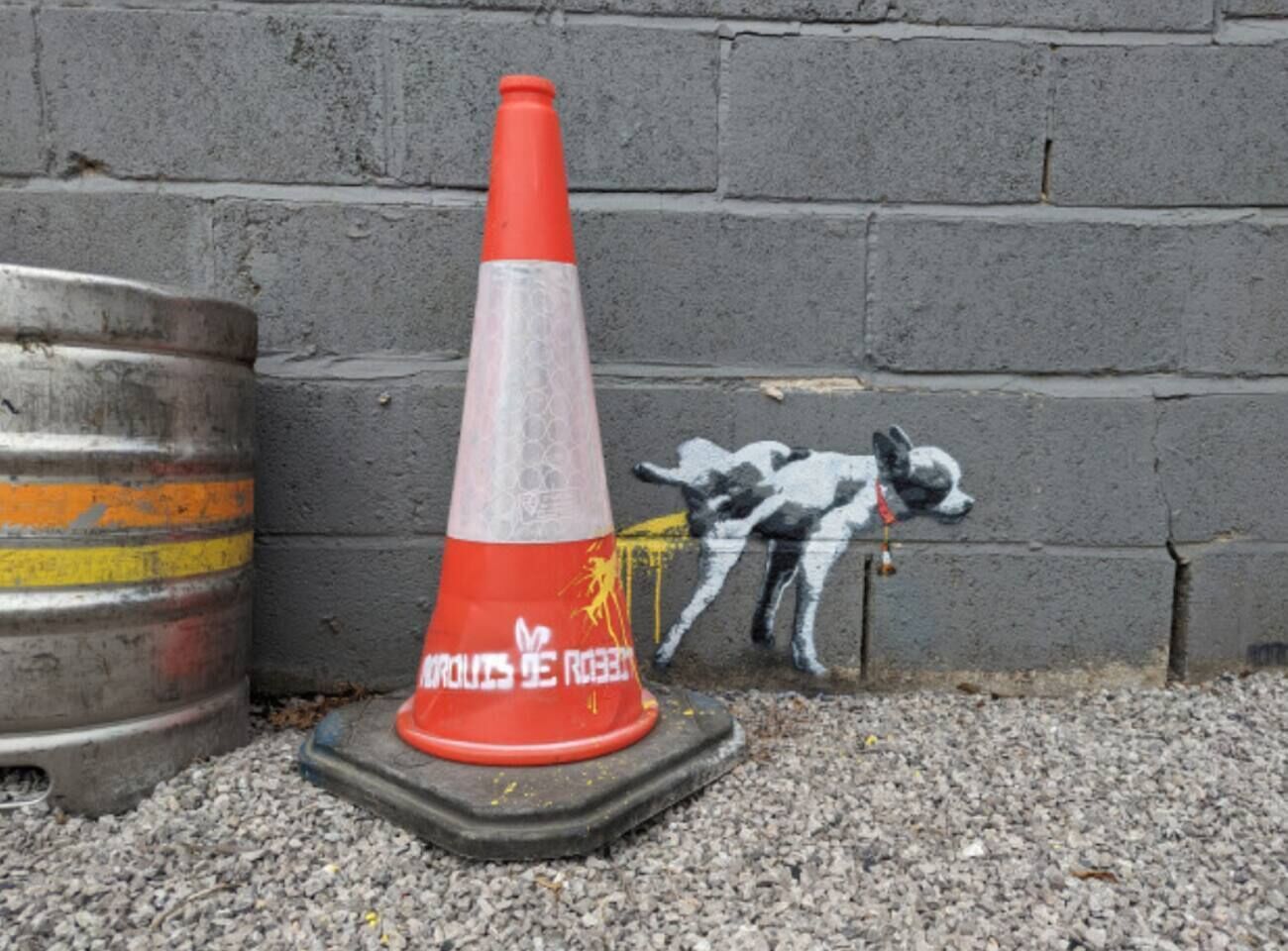 Un cono stradale con graffiti accanto a un muro in cemento.