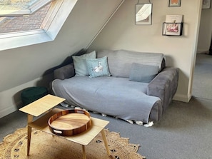 A cozy loft bedroom with a grey sofa, a small wooden side table, and a woven rug.