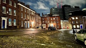 A nighttime urban street with brick buildings, a wet cobblestone road, and a modern building with cranes in the background. - Gracious Apartment in Historic Sheffield Georgian Quarter (Sheffield City Centre)