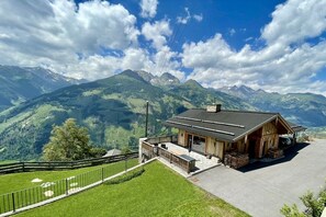 Eine Berglodge mit Holzfassade, einer überdachten Terrasse und Blick auf die umliegenden Berge.