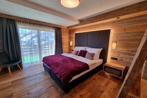 Un dormitorio con una cama grande, paredes de madera, una ventana con cortinas y una mesita de noche pequeña.