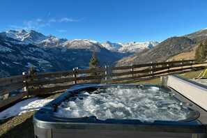 Un jacuzzi con un cerco de madera en primer plano y un paisaje montañoso al fondo.