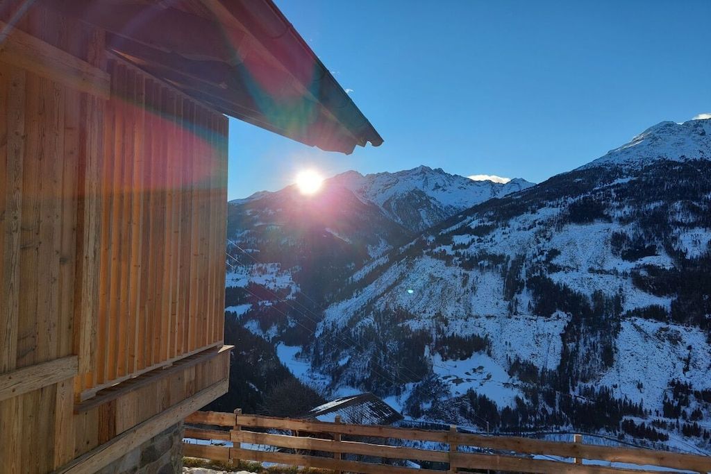 A wooden cabin with a view of snow-covered mountains and a clear sky.