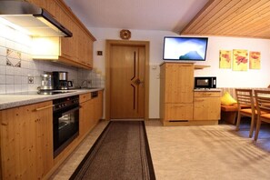 A compact kitchen with wooden cabinets, a stove, a microwave, and a TV on the wall. - Holiday apartment in Kappl with swimming pool (Kappl)