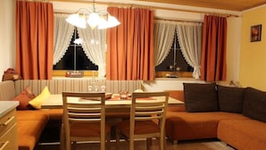 Ein gemütliches Wohnzimmer mit Esstisch, Holzstühlen, einer Couch und einem Fenster mit Vorhängen.