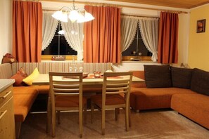 A cozy living room with a dining table, wooden chairs, a sofa, and a window with curtains. - Holiday apartment in Kappl with swimming pool (Kappl)