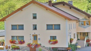 Ein zweistöckiges Gebäude mit geneigtem Dach, mehreren Fenstern und einem Hauseingang mit Treppe.