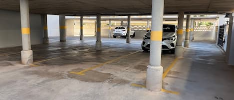 A parking garage with concrete pillars, yellow lines, and a white car parked.