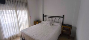 Un lit simple avec une tête de lit, deux tables de chevet et une fenêtre avec des rideaux légers.