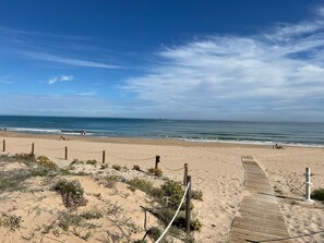 A sandy beach with a wooden boardwalk leading to the water, a rope barrier, and a clear sky. - Beachfront apartment, stunning views. (Daimús)