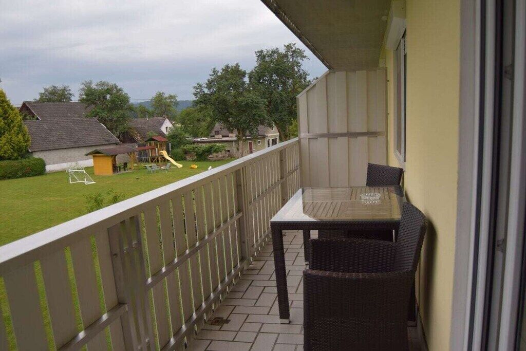 A balcony with a table and chairs, a view of a grassy yard with a playground, and houses in the background.