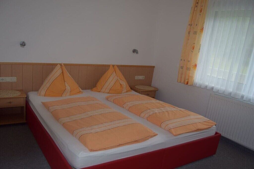 Ein Doppelbett mit rotem Untergestell, zwei Nachttische und ein Fenster mit Vorhängen.
