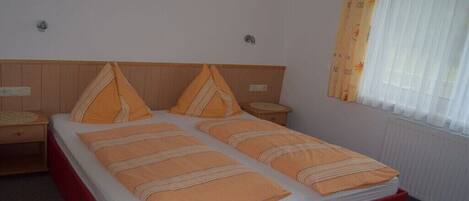 A double bed with a red base, two bedside tables, and a window with curtains.