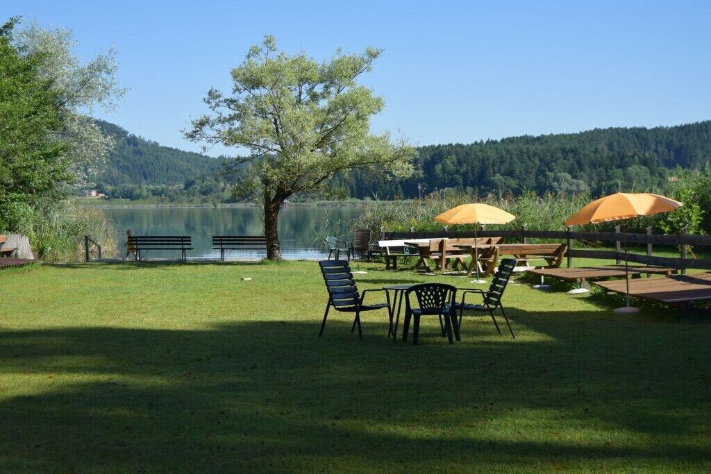 An outdoor seating area with tables and chairs, surrounded by a grassy lawn and a lake view.