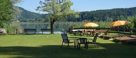 An outdoor seating area with tables and chairs, surrounded by a grassy lawn and a lake view.