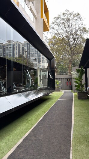 Un edificio moderno con fachada de vidrio, un sendero y una pequeña zona ajardinada con césped artificial.