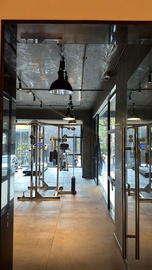 Un gimnasio con equipamiento de ejercicio, ventanas amplias y techo de hormigón.