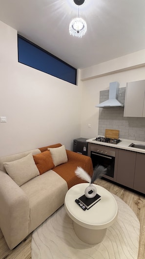 A modern living room with a sofa, a round coffee table, and a kitchen area with a stove and cabinets. - Stylish 1-Bed at Wilma Towers | Fast Wi-Fi & City and pool views (Nairobi)