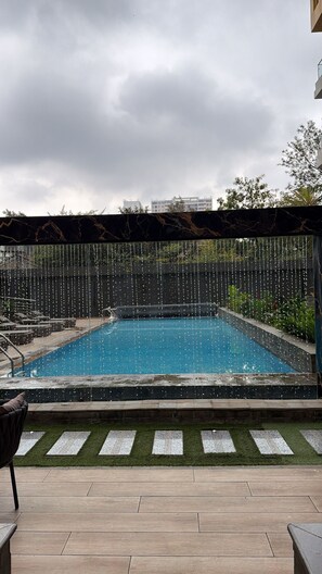 Una piscina con fuente acuática, rodeada por un muro bajo y un césped con piedras para pisar.