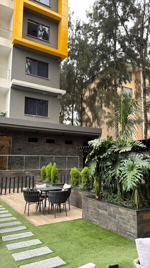 A modern building with a balcony, a patio with outdoor furniture, and a garden area with various plants. - Stylish 1-Bed at Wilma Towers | Fast Wi-Fi & City and pool views (Nairobi)