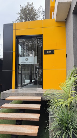Un edificio moderno con fachada amarilla, acceso de vidrio y un cartel que indica un gimnasio.
