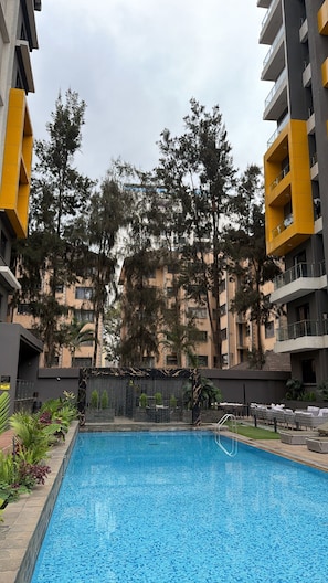 A swimming pool surrounded by trees and multi-story buildings with balconies. - Stylish 1-Bed at Wilma Towers | Fast Wi-Fi & City and pool views (Nairobi)