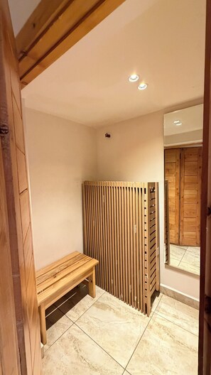 Een badkamer met een houten bankje, een verticale houten wand en een betegelde vloer.