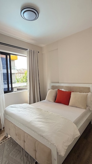 Ein Hotelzimmer mit einem Bett, einem Fenster mit Vorhängen und Blick auf Gebäude.