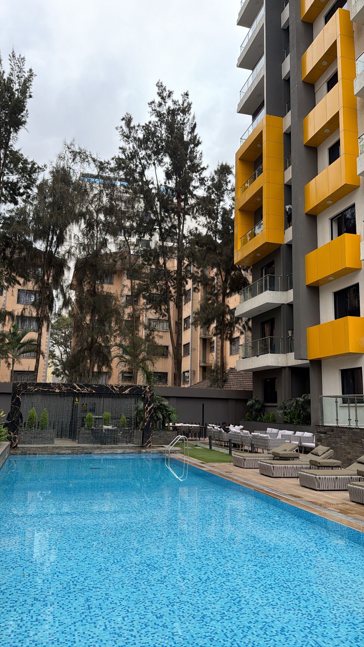 A swimming pool with a tiled deck area, surrounded by a multi-story building with balconies.