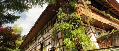 A traditional half-timbered building with a sloped roof, surrounded by potted plants and a cobblestone pathway.