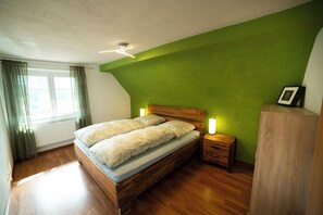A bedroom with a wooden bed, bedside tables, a nightstand with a lamp, and a radiator. - Vrbo Property (Ottenhöfen im Schwarzwald)