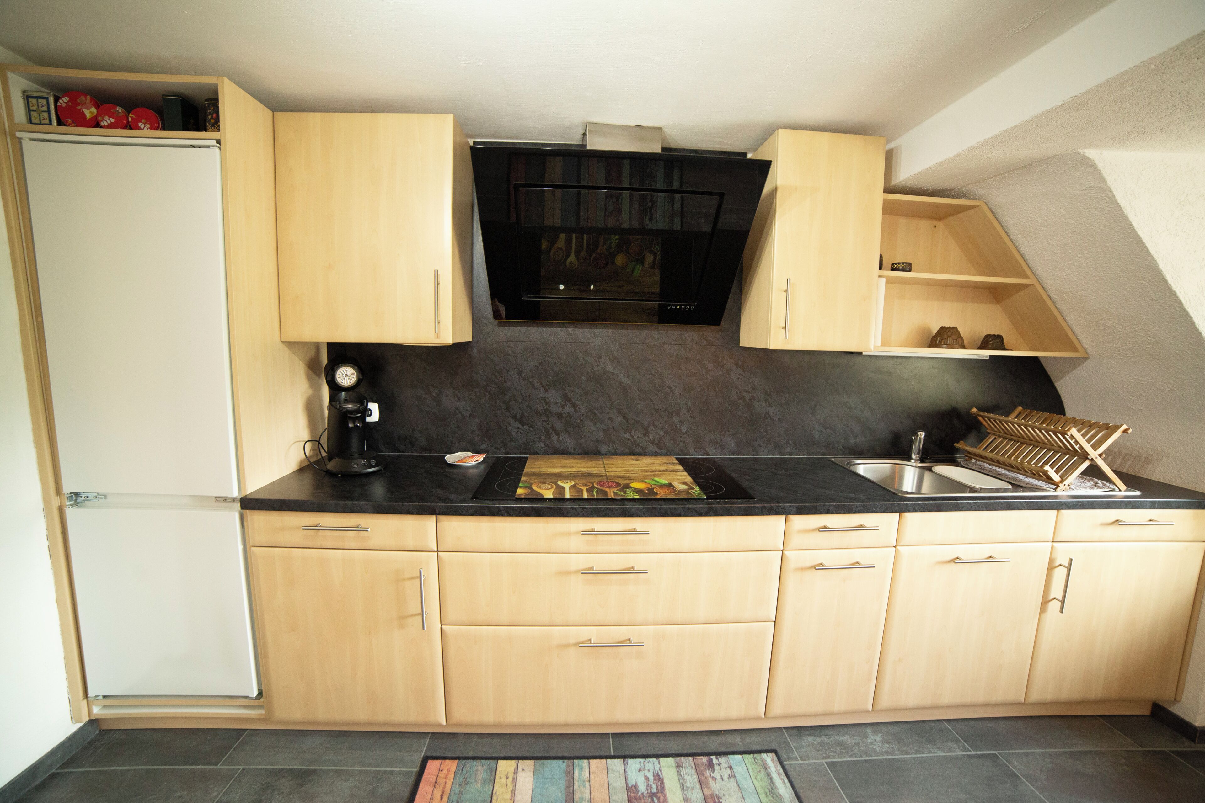 Eine kleine Küche mit schwarzer Arbeitsplatte, Holzschränken, einem eingebauten Backofen und einem Spülbecken.