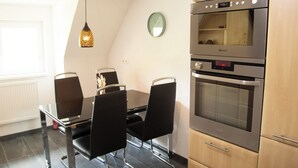 Une cuisine moderne dotée d’un four encastré, d’une table à manger avec des chaises et d’un luminaire suspendu.
