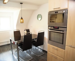 A modern kitchen with a built-in oven, a dining table with chairs, and a pendant light. - Vrbo Property (Ottenhöfen im Schwarzwald)