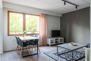 Una sala de estar moderna con comedor, televisor y un amplio ventanal con vistas a árboles.