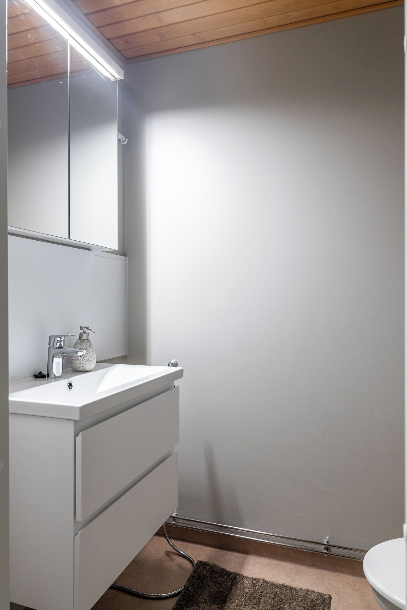 Un baño con tocador blanco, espejo, grifo y retrete.