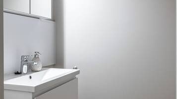 Un baño con tocador blanco, espejo, grifo y retrete.