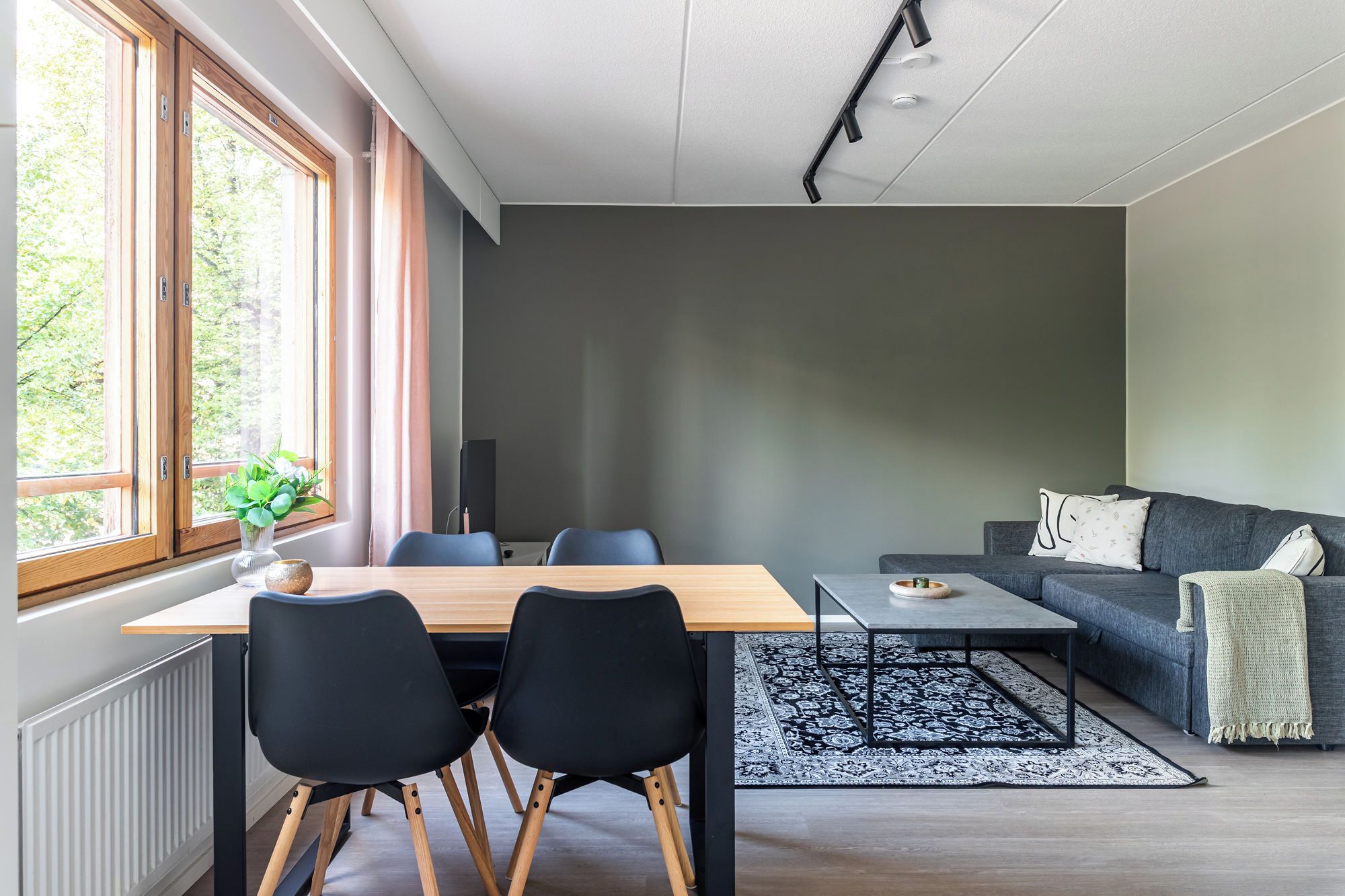 Un salon moderne comprenant un coin repas, de grandes fenêtres, un canapé gris et un tapis noir et blanc.