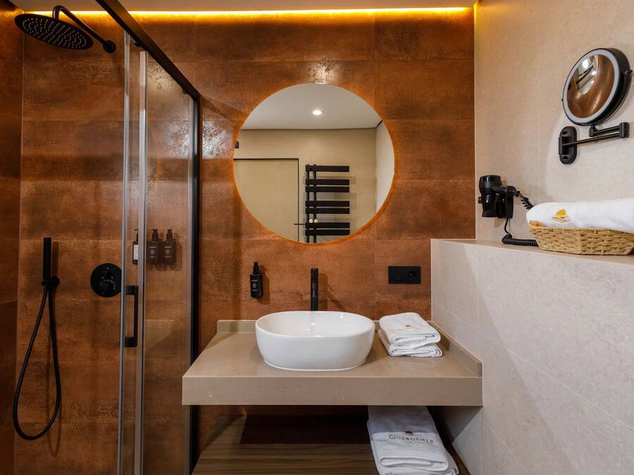 A modern bathroom with a glass-enclosed shower, a round mirror, a white sink, and a towel rack with a folded towel.