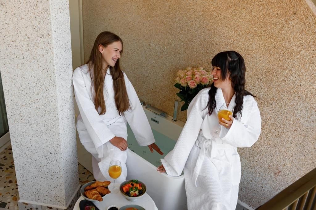 Dos personas vestidas de blanco de pie junto a una mesa con alimentos y bebidas para el desayuno.
