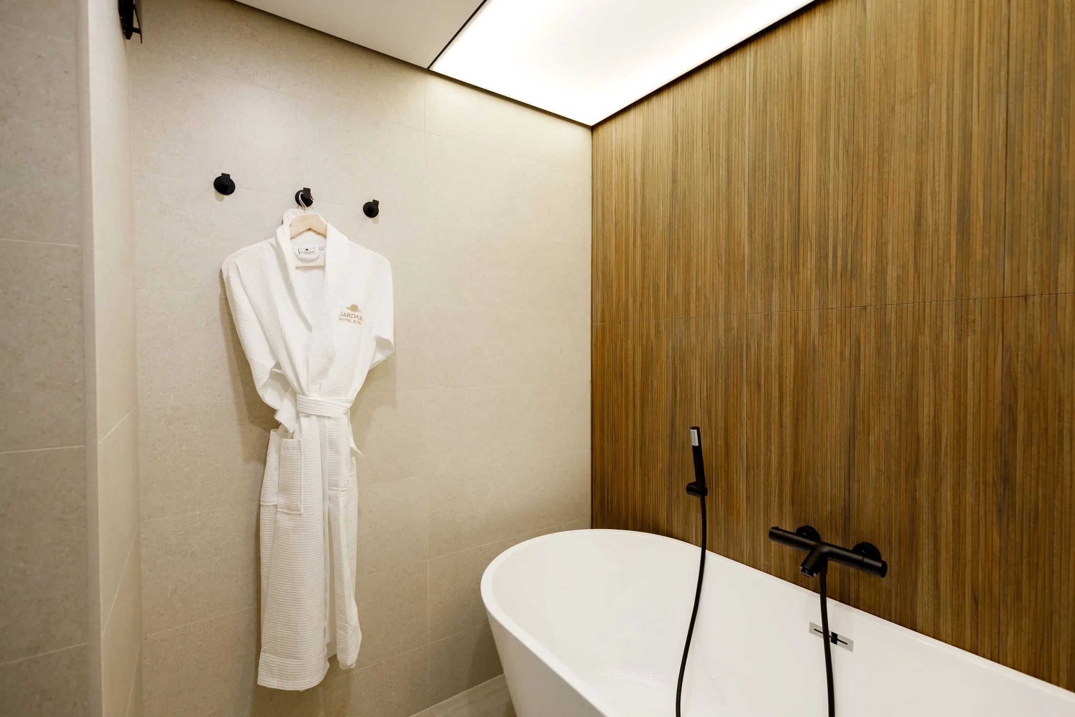 Un baño moderno con una bañera independiente, un perchero con una bata blanca y un panel de pared de madera.