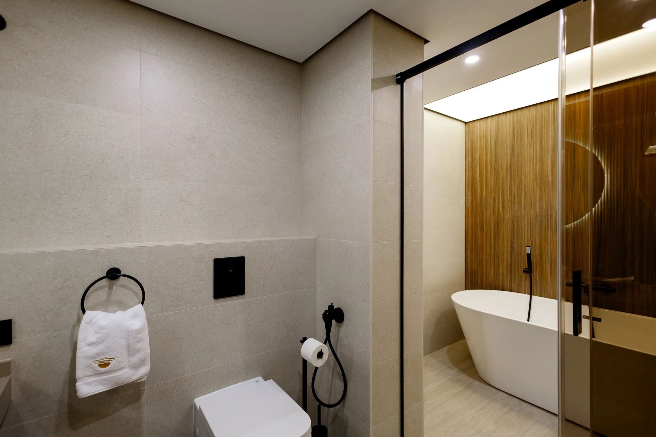 Uma casa de banho moderna com cabine de duche em vidro, uma banheira branca e um porta-toalhas com toalha.