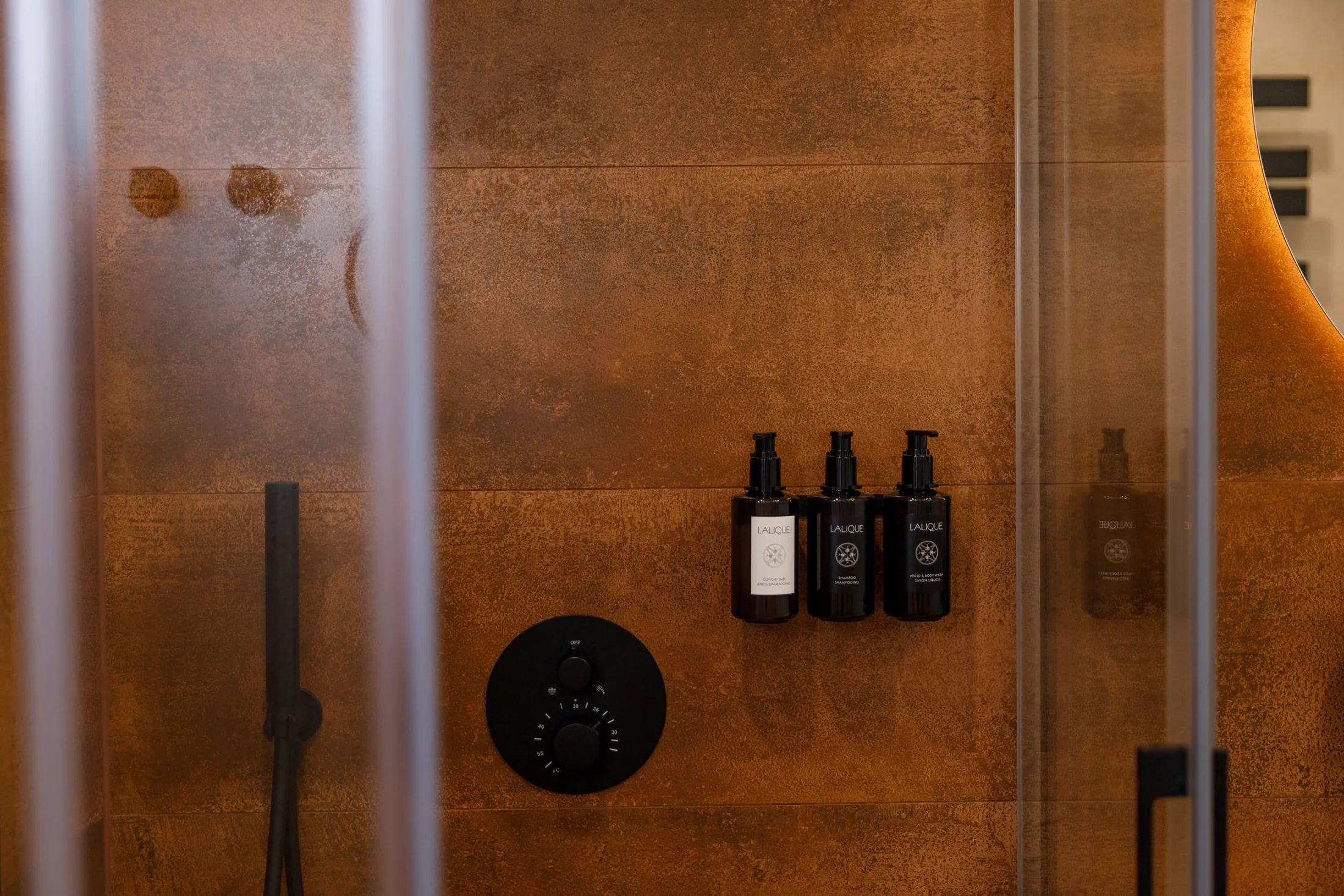A shower area with a control panel and three bottles of L'ALIQUE shampoo.